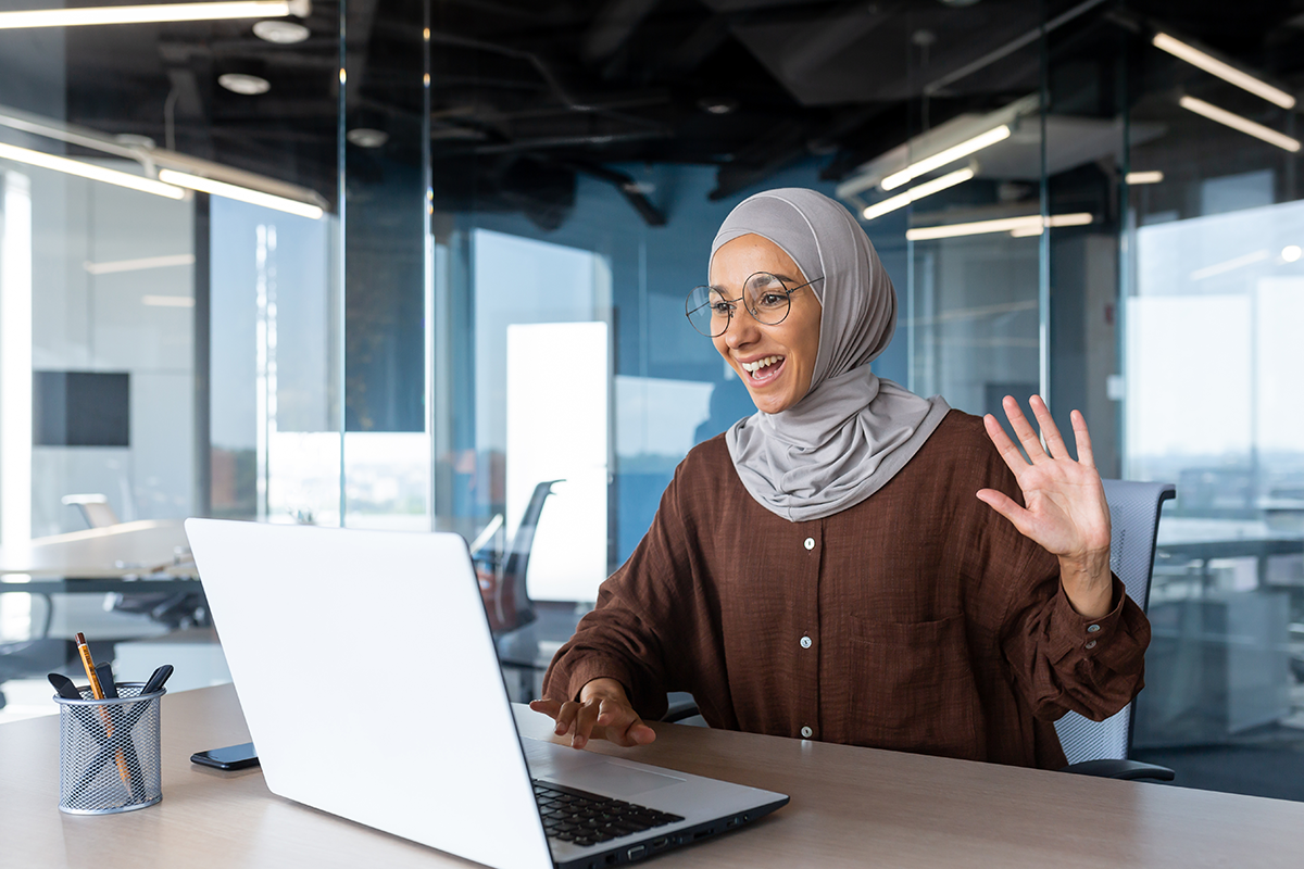 An Ad Astra Video Interpreter smiles at a laptop while waving. She is visibly excited.